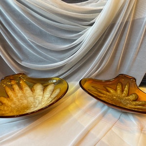 May include: Two amber glass bowls with a unique swirl design. The bowls are shaped like seashells and have a glossy finish.