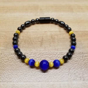 May include: A black and blue beaded bracelet with a magnetic clasp. The bracelet has yellow beads with a cat's eye effect.