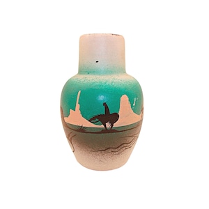 May include: A turquoise and white ceramic vase with a silhouette of a bird and a desert landscape.