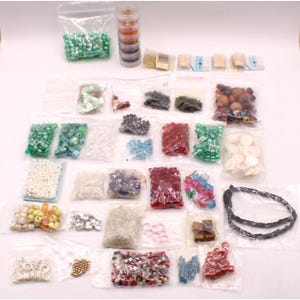 May include: A collection of assorted craft beads and jewelry components packaged in clear plastic bags and a cylindrical stackable container. The set includes various shapes, sizes, and colors of glass, plastic, and wooden beads, along with metal findings.