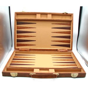 May include: Open brown leather backgammon set with a tan playing surface and dark brown and tan triangles. The set is rectangular with a handle and metal clasps. The interior is lined with tan felt.