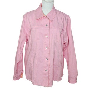 May include: A pink denim button-down shirt with long sleeves and a pointed collar. The shirt has a row of clear rhinestones down the front placket and along the pockets.