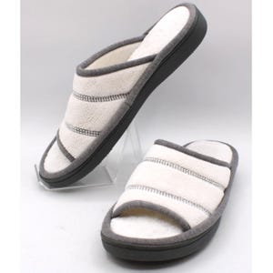 May include: A pair of open-toe slippers featuring a cream-colored, textured upper with horizontal stitching details. The slippers have dark gray trim along the edges and a solid dark gray sole, providing a neutral color palette and simple design.