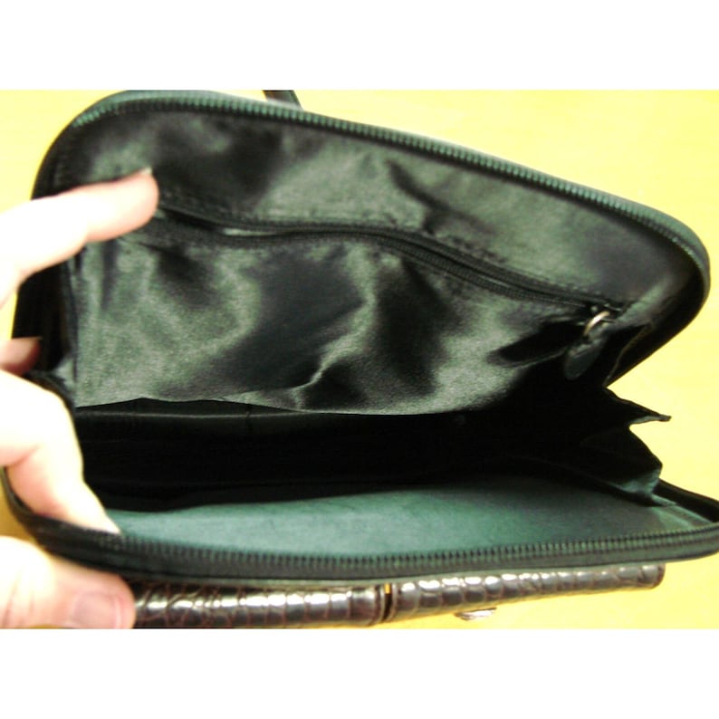 Puede incluir: Vista abierta de una cartera marr&oacute;n oscuro con un patr&oacute;n texturizado similar al de un cocodrilo. El interior es negro con un bolsillo con cremallera. La cartera est&aacute; abierta, revelando el interior.