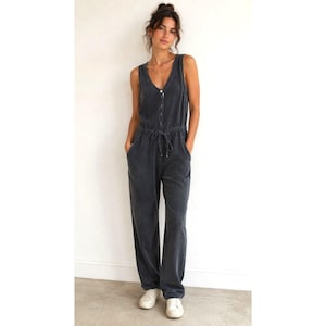 May include: A charcoal gray sleeveless jumpsuit featuring a V-neckline, a button-down front placket, and a drawstring waist tie. The garment has a relaxed fit with wide-leg trousers and is crafted from a soft, washed-out fabric texture.