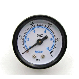 May include: A black and white pressure gauge with a blue needle and a white face. The gauge reads up to 10 kgf/cm² and has a black bezel. The gauge is labeled "MC" and "MPa".