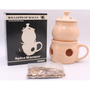 May include: A peach-colored ceramic spice warmer with a lid, handle, and air holes, next to a box that reads "WILLIAMS OF WALES Spice Warmer." A small bag of spices is in front of the warmer.