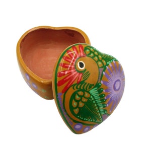 May include: A heart-shaped ceramic trinket box with a painted design of a bird with green and purple flowers. The lid is open and the inside of the box is visible.