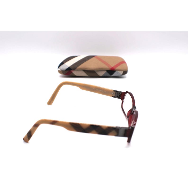 May include: Eyeglasses with a burgundy frame and light brown arms. The arms have a brown and tan plaid pattern. A matching plaid eyeglasses case is in the background.