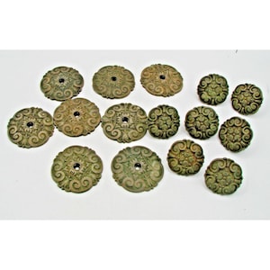May include: A collection of antique bronze-colored decorative hardware pieces. The pieces are circular with ornate, swirling patterns and a central hole. The collection includes various sizes, all with a weathered, aged appearance.