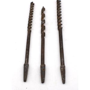 May include: Three vintage metal auger drill bits arranged vertically. Each tool features a dark, weathered finish with a spiral fluted shaft and a tapered, square-shaped shank at the base for attachment to a brace or hand drill handle.