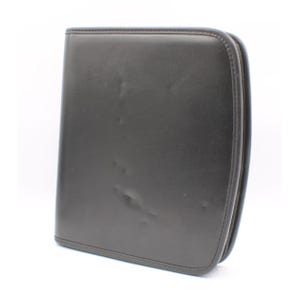 May include: A dark brown leather portfolio with a zipper closure. The rectangular case has a slightly textured surface and rounded edges. The portfolio is designed to hold documents and other items.