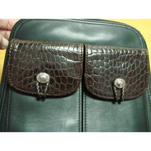 Puede incluir: Bolso de cuero negro con dos bolsillos marrones con textura de cocodrilo. Cada bolsillo tiene un cierre de bot&oacute;n plateado con un detalle trenzado decorativo. El bolso tiene cierre de cremallera y es probablemente un bolso de hombro o un bolso de mano.