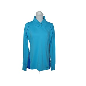 May include: A bright blue long-sleeve pullover shirt featuring a high collar with three small green buttons, long sleeves with thumb holes, and contrasting dark blue side panels. The garment has a smooth texture and a small green logo at the hem.