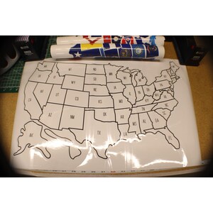 May include: A large white map of the United States with state outlines and abbreviations. The map is packaged in clear plastic. Rolled-up decorative paper with patriotic designs is visible in the background.