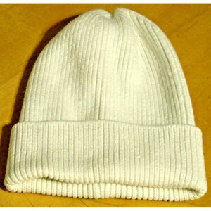 May include: A white knitted beanie with a ribbed texture. The beanie has a folded brim.