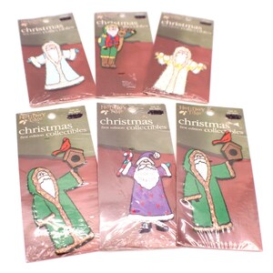 May include: Six Holiday Time Christmas first edition collectible pins on individual cardboard backing cards. The pins feature various Santa Claus figures in different colored robes, some holding birdhouses with red birds or candy canes.