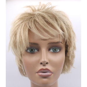 May include: A mannequin head with a short, layered blonde wig. The wig has a natural-looking style with textured layers and a slightly tousled appearance. The mannequin has green eyes and a neutral expression.