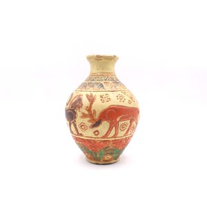May include: A small, antique-style vase with a cream-colored base and a narrow neck. The vase features hand-painted illustrations of deer and figures in shades of red, brown, and blue. The base has a band of green and orange floral designs.