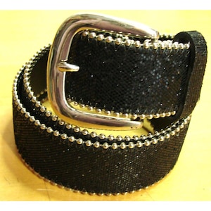 May include: A black belt with a silver buckle. The belt is covered in a sparkly, mesh-like material and is trimmed with small, silver-colored beads. The buckle is a shiny, curved design.