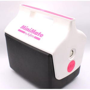 May include: A white and black MiniMate cooler by Igloo with a pink handle and accents. The cooler has the words "MiniMate" and "by igloo" printed in pink. The Igloo logo is also printed in pink on the side.