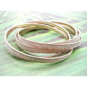 May include: Set of four gold-tone bangles with a sparkly finish. The bangles are stacked on top of each other.