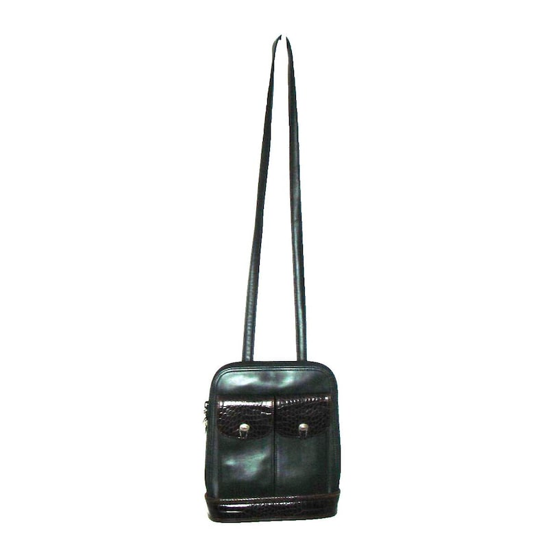 Puede incluir: Bolso bandolera de cuero negro con dos bolsillos delanteros con solapa con textura de cocodrilo y herrajes plateados. El bolso tiene una correa larga y fina y una base marr&oacute;n oscuro.