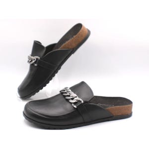 May include: Black leather slip-on shoes with silver chain detail. The shoes have a cork footbed and a black sole. One shoe is positioned upright, while the other is flat on the surface.