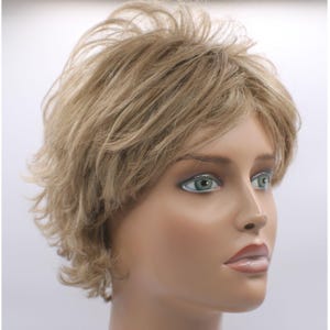 May include: A short, layered wig in shades of blonde and light brown. The wig features a choppy, textured style with a side part. The hair is styled to frame the face, creating a natural and voluminous look. The wig is displayed on a mannequin head.
