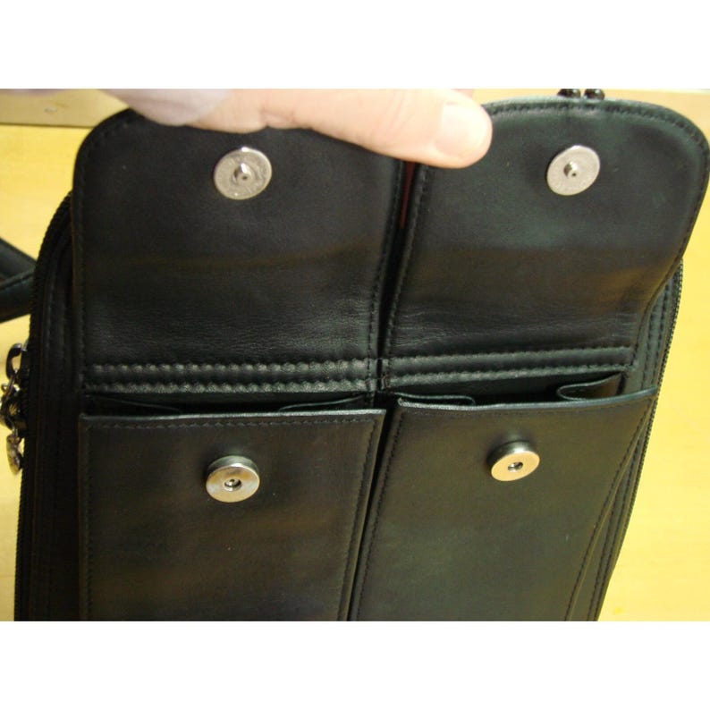 Puede incluir: Bolso de mano de cuero negro con m&uacute;ltiples compartimentos. El bolso presenta un cierre de solapa con botones a presi&oacute;n plateados. El interior revela varios bolsillos, mostrando el dise&ntilde;o organizativo del bolso. El bolso est&aacute; dise&ntilde;ado para llevar lo esencial.