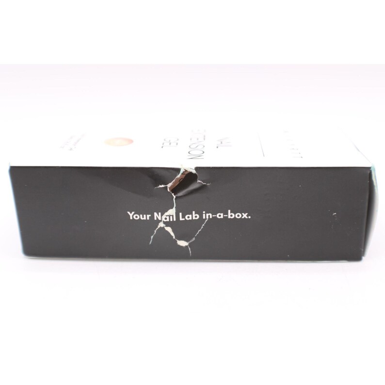 Op de afbeelding: Een zwarte doos met de tekst "Your Nail Lab in-a-box." De doos heeft een scheur aan de zijkant. De bovenkant van de doos is wit met wat tekst en een ontwerp.