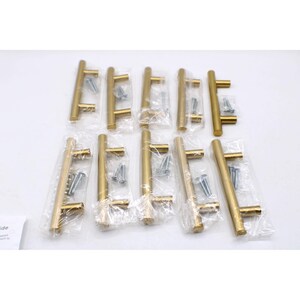 May include: A set of ten gold-toned T-bar cabinet pulls, each individually wrapped in clear plastic packaging. Each handle features a cylindrical bar with two perpendicular mounting posts and includes two silver-colored metal screws for installation.