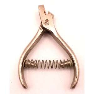 May include: A vintage metal pliers tool with a spring and curved handles. The pliers are silver-toned and show signs of wear. The tool is designed for cutting or shaping materials. The spring is a coiled design.