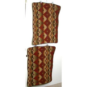 May include: Two decorative pillow covers with a Southwestern-inspired geometric pattern in shades of brown, red, and beige. The covers are hanging on a white wall.