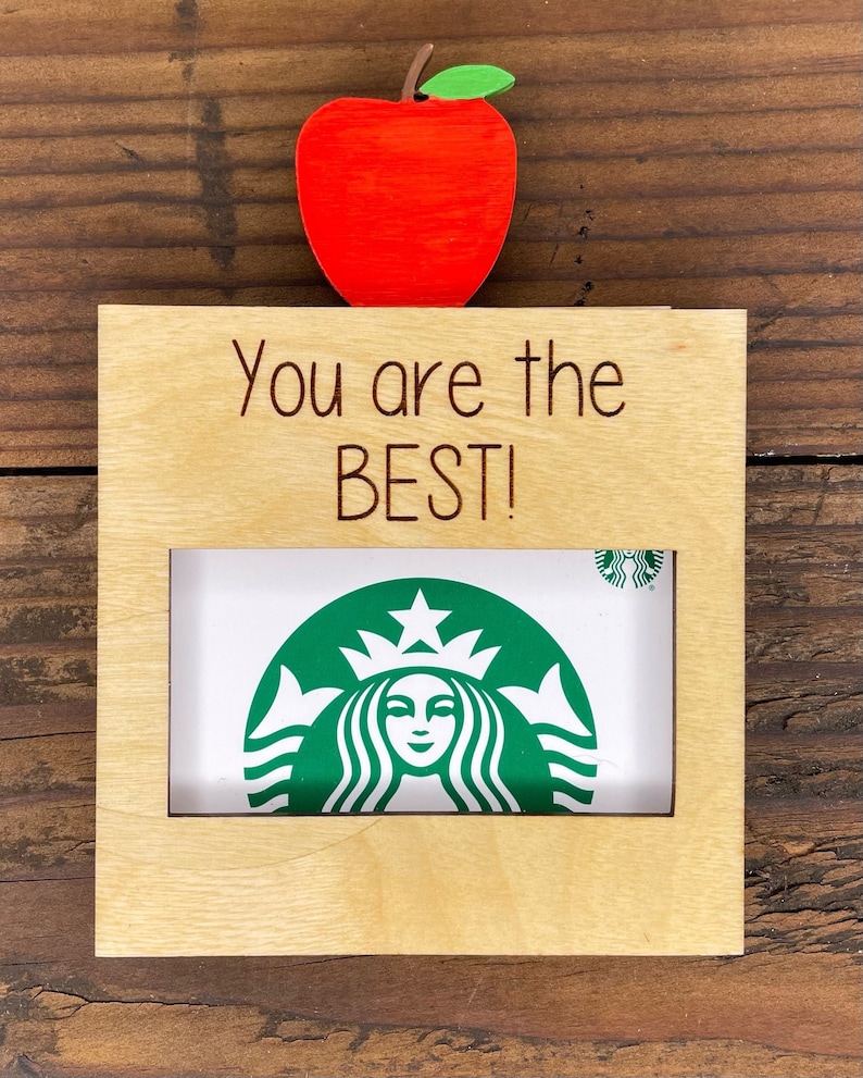 Pu&ograve; includere: Una cornice in legno con una mela rossa in cima. La cornice ha un ritaglio per una foto e il testo "You are the BEST!" &egrave; inciso sul davanti.