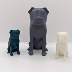 Puede incluir: Tres figuritas de perro pug geom&eacute;tricas impresas en 3D de diferentes tama&ntilde;os. El pug m&aacute;s grande es gris, el pug de tama&ntilde;o mediano es azul verdoso y el pug m&aacute;s peque&ntilde;o es blanco.
