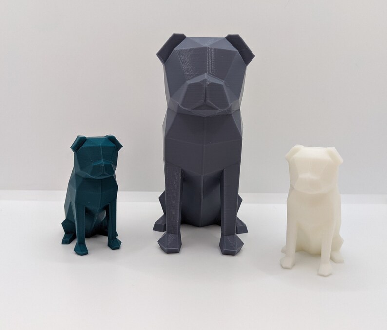 Puede incluir: Tres figuritas de perro pug geom&eacute;tricas impresas en 3D de diferentes tama&ntilde;os. El pug m&aacute;s grande es gris, el pug de tama&ntilde;o mediano es azul verdoso y el pug m&aacute;s peque&ntilde;o es blanco.