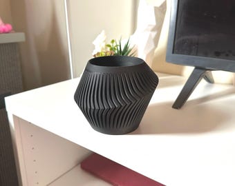 May include: A black, geometric planter with a wavy, textured design. The planter is made of a hard, durable material and has a wide, round opening.