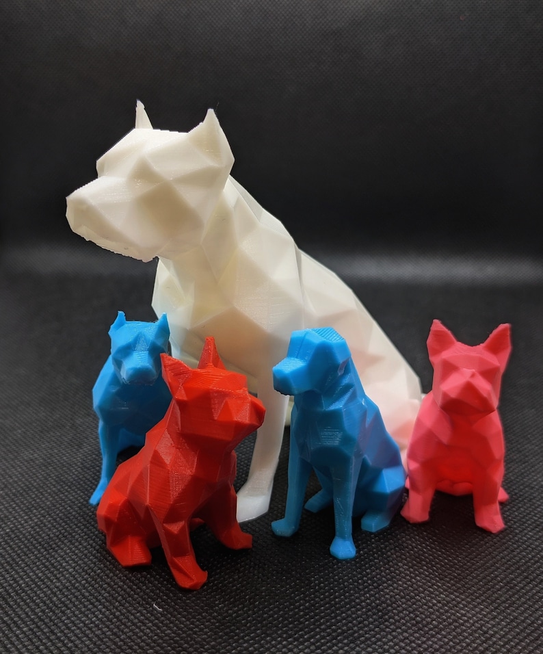 Puede incluir: Cuatro figuritas de perro de bajo pol&iacute;gono, una blanca, una roja y dos azules. El perro blanco est&aacute; sentado y los otros tres est&aacute;n de pie.