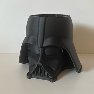 May include: A black plastic Darth Vader head planter. The planter is shaped like Darth Vader's head and has a hole in the top for planting.