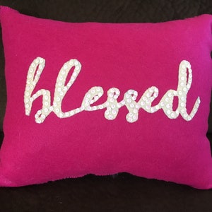 May include: A pink throw pillow with the word "blessed" spelled out in white sequins.