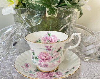 May include: A white teacup and saucer with a pink floral pattern. The cup has a gold rim and the saucer has a scalloped edge.