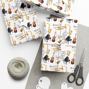 Puede incluir: Papel de regalo blanco con un patrón de instrumentos musicales, incluyendo pianos, violines, trompetas y saxofones. Los regalos están atados con hilo y tienen etiquetas en blanco. También se ven un ovillo de hilo, unas tijeras y etiquetas en blanco.
