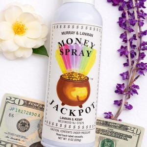 May include: A light blue spray bottle labeled "Money Spray Jackpot" with a pot of gold graphic. The bottle is next to two twenty-dollar bills, a white flower, and purple flowers. The bottle contains 8 oz (226g) of product.