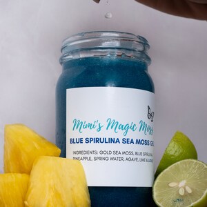 K&ouml;nnte beinhalten: Ein blaues Glasgef&auml;&szlig; mit einem wei&szlig;en Etikett, auf dem "Mimi's Magic Moss Blue Spirulina Sea Moss Gel" steht. Die Zutaten sind auf dem Etikett aufgelistet: "Gold Sea Moss, Blue Spirulina, Ananas, Quellwasser, Agave, Limette & Liebe". Neben dem Gef&auml;&szlig; liegen Ananasst&uuml;cke und Limettenscheiben.