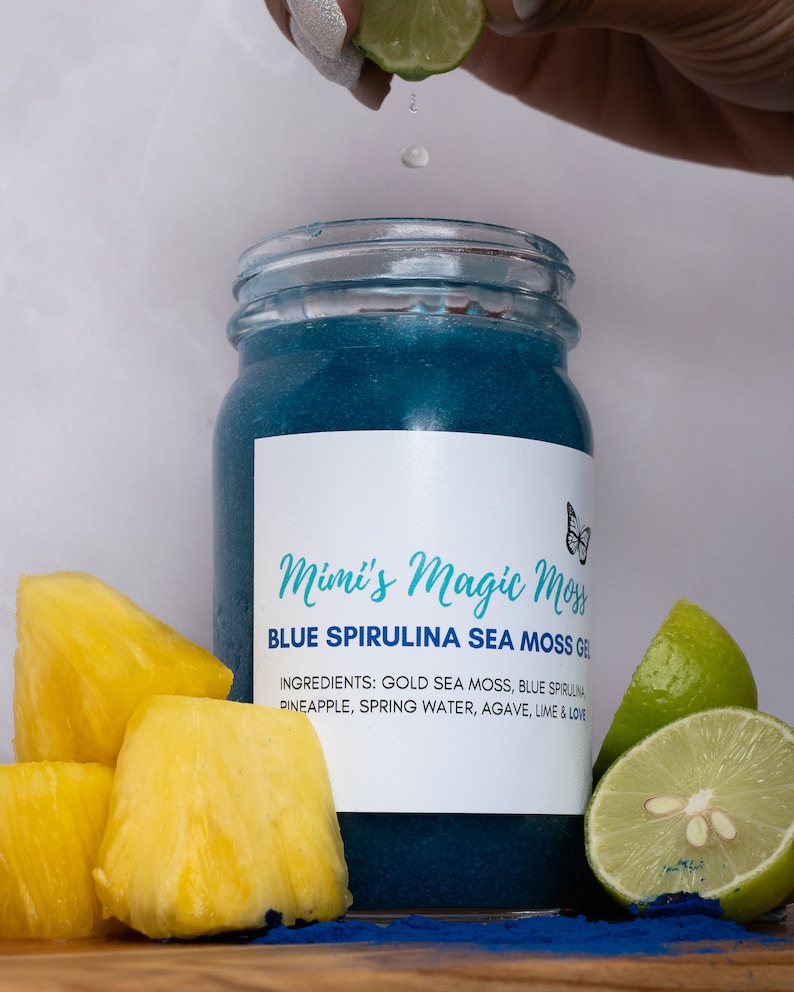 K&ouml;nnte beinhalten: Ein blaues Glasgef&auml;&szlig; mit einem wei&szlig;en Etikett, auf dem "Mimi's Magic Moss Blue Spirulina Sea Moss Gel" steht. Die Zutaten sind auf dem Etikett aufgelistet: "Gold Sea Moss, Blue Spirulina, Ananas, Quellwasser, Agave, Limette & Liebe". Neben dem Gef&auml;&szlig; liegen Ananasst&uuml;cke und Limettenscheiben.