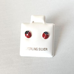 May include: A pair of sterling silver ladybug stud earrings. Each earring features a red and black ladybug design. The earrings are displayed on a white card with the words "STERLING SILVER" printed on it.