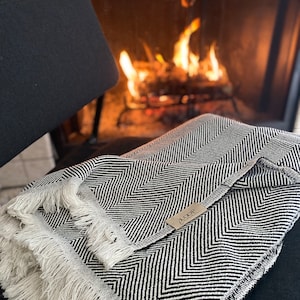 May include: Black and white chevron patterned throw blanket with a fringe border. The blanket has a small white tag with the text "A COOP" on it.