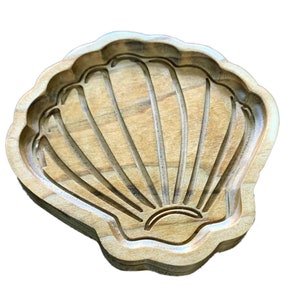May include: A wooden seashell-shaped tray with a carved design. The tray is light brown in color and has a smooth, polished finish.