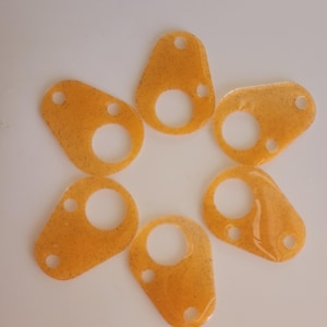 May include: Six amber-colored, translucent, teardrop-shaped flat components arranged in a circular pattern. Each piece features a large circular cutout in the center, a smaller circular hole at the top, and a tiny circular hole at the side.